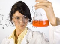 1105866-young-beauty-chemist-girl-in-white-apron-holding-beaker-with-orange-liquid-wearing-goggles-gray-back